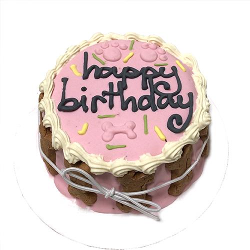 A pink birthday cake for dogs, made with peanut butter and apples, featuring a dense texture and a candle on top for celebration.