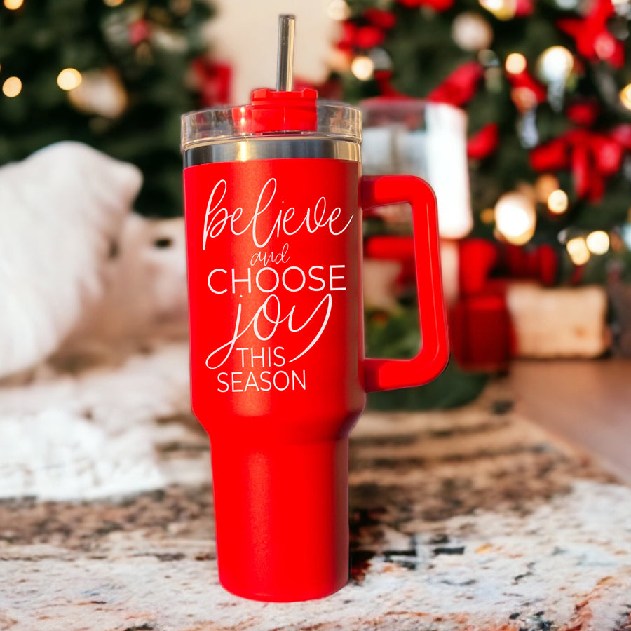 Believe + Joy 40oz insulated mug with a cheerful design and inspirational quote, featuring a lid, straw, and handle.