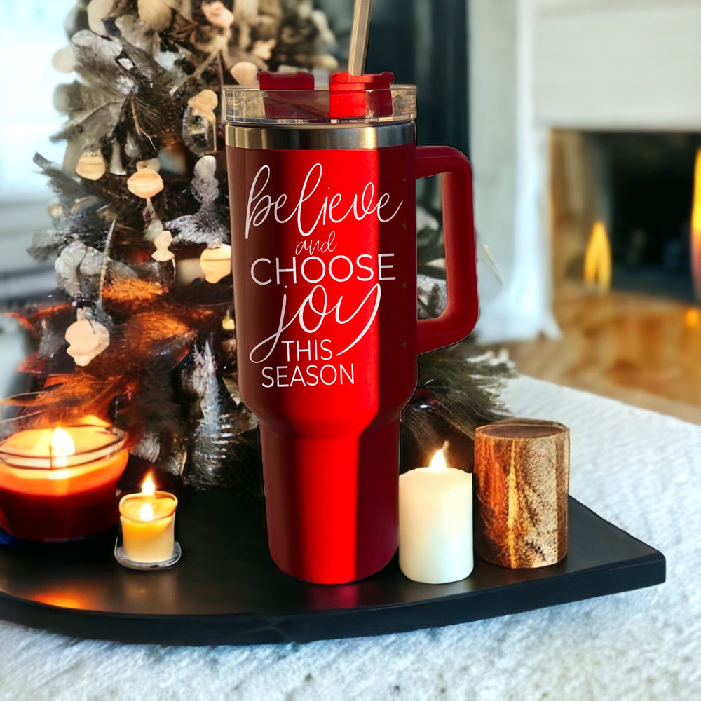 Believe + Joy 40oz insulated mug with a cheerful design and inspirational quote, featuring a lid, straw, and handle.