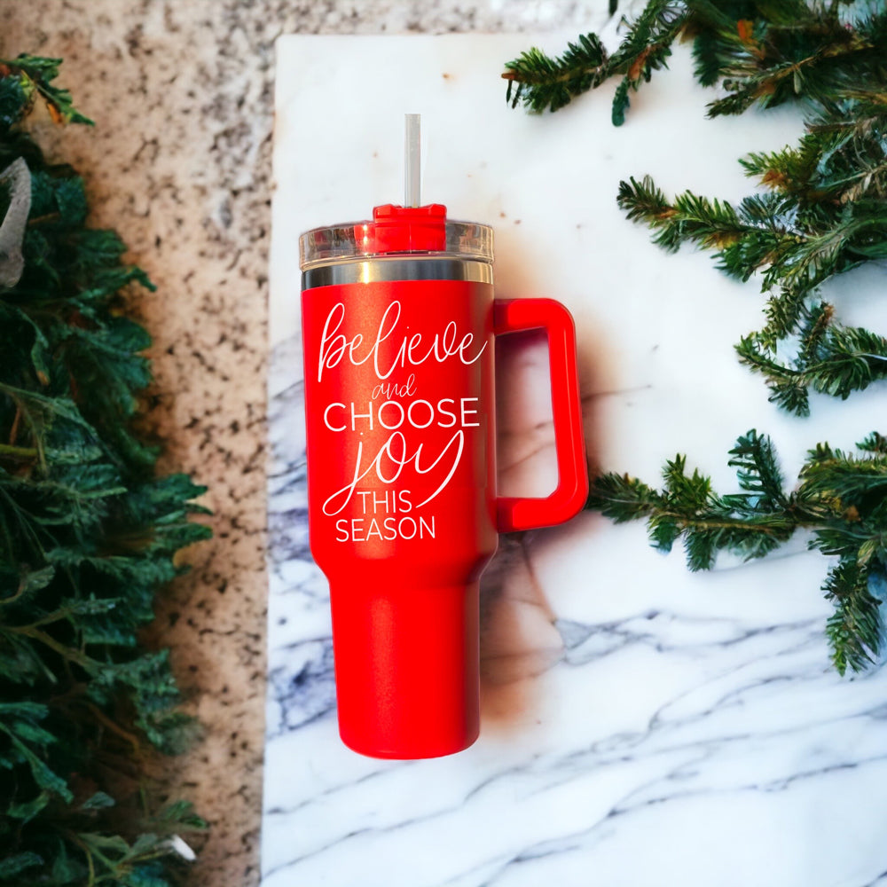 Believe + Joy 40oz insulated mug with a cheerful design and inspirational quote, featuring a lid, straw, and handle.