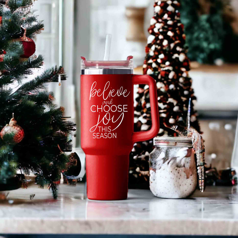 Believe + Joy 40oz insulated mug with a cheerful design and inspirational quote, featuring a lid, straw, and handle.