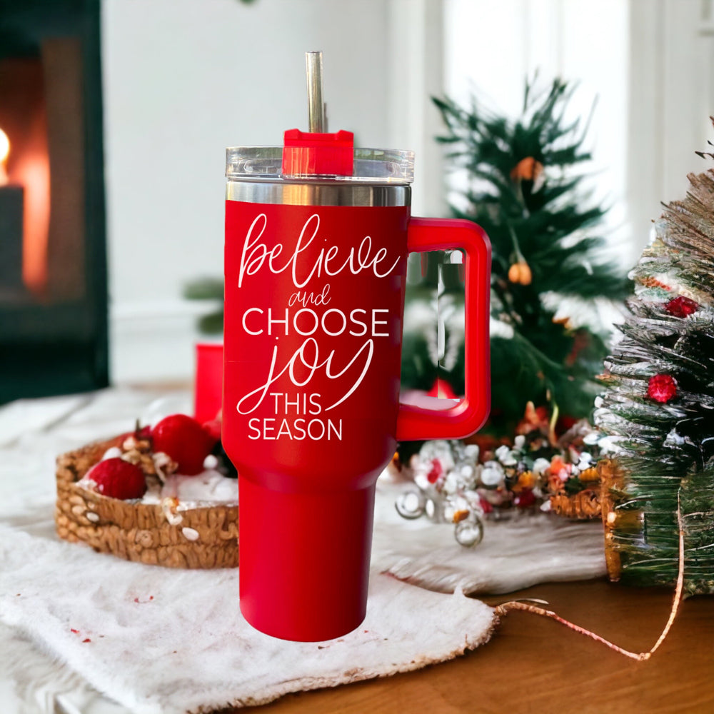 Believe + Joy 40oz insulated mug with a cheerful design and inspirational quote, featuring a lid, straw, and handle.