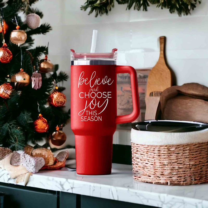 Believe + Joy 40oz insulated mug with a cheerful design and inspirational quote, featuring a lid, straw, and handle.