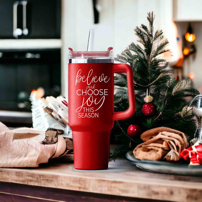 Believe + Joy 40oz insulated mug with a cheerful design and inspirational quote, featuring a lid, straw, and handle.