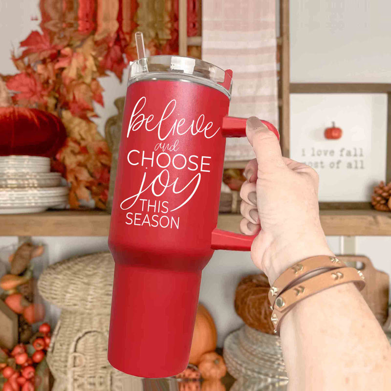 Believe + Joy 40oz insulated mug with a cheerful design and inspirational quote, featuring a lid, straw, and handle.