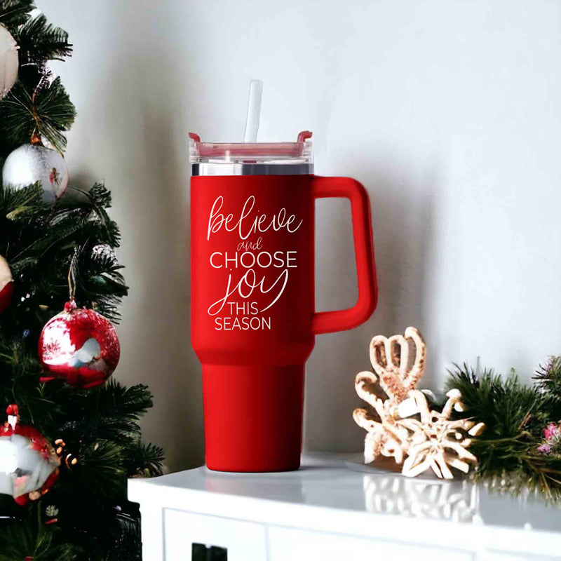 Believe + Joy 40oz insulated mug with a cheerful design and inspirational quote, featuring a lid, straw, and handle.