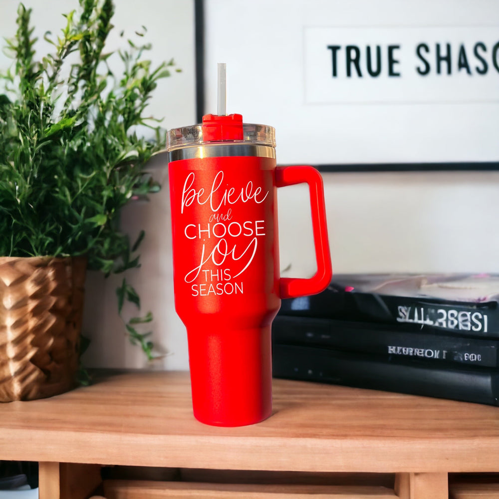 Believe + Joy 40oz insulated mug with a cheerful design and inspirational quote, featuring a lid, straw, and handle.