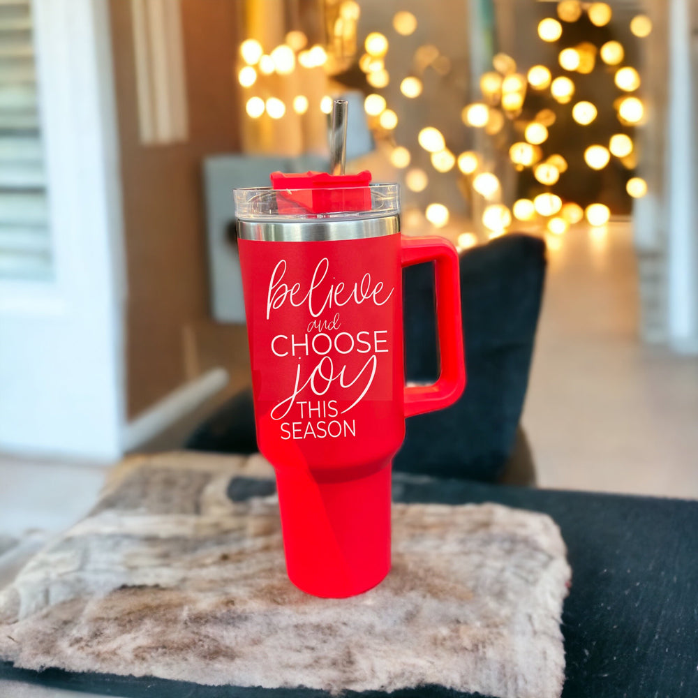 Believe + Joy 40oz insulated mug with a cheerful design and inspirational quote, featuring a lid, straw, and handle.