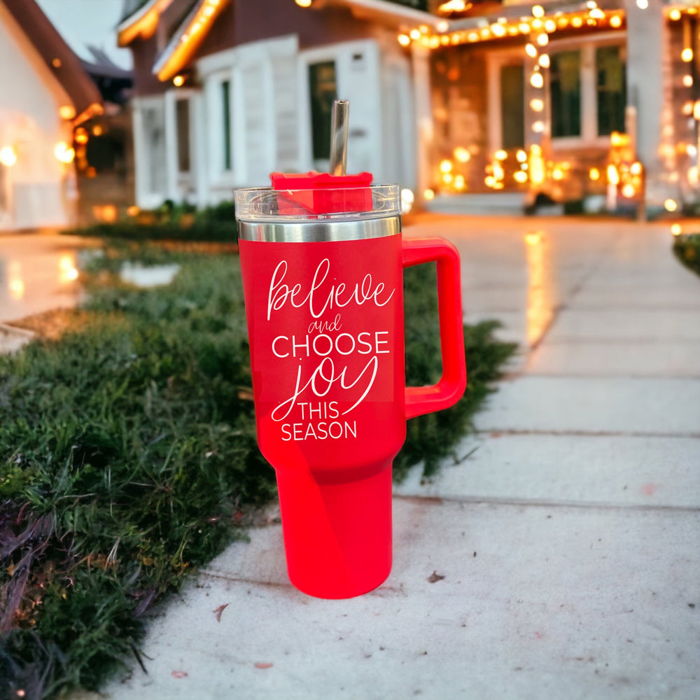 Believe + Joy 40oz insulated mug with a cheerful design and inspirational quote, featuring a lid, straw, and handle.