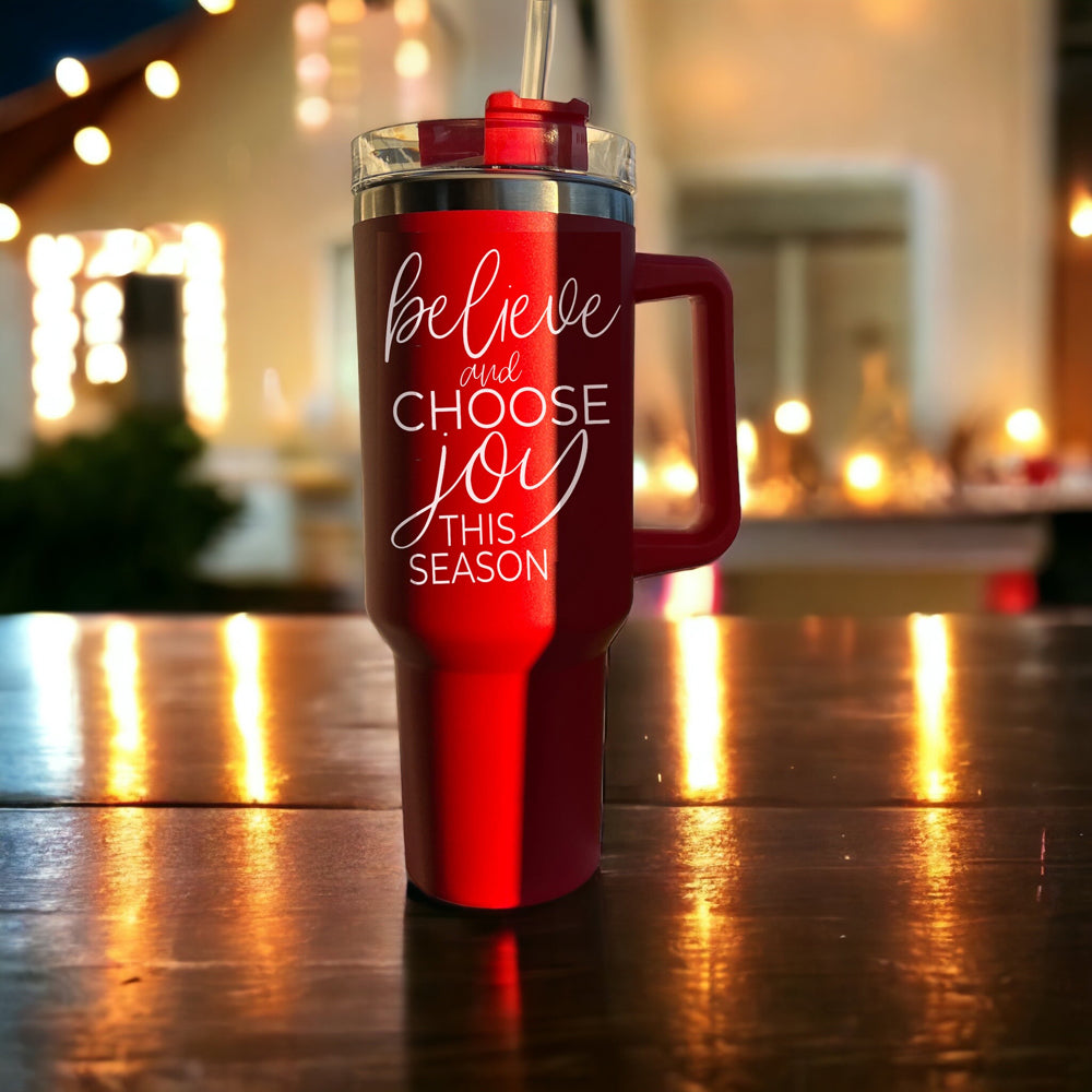 Believe + Joy 40oz insulated mug with a cheerful design and inspirational quote, featuring a lid, straw, and handle.