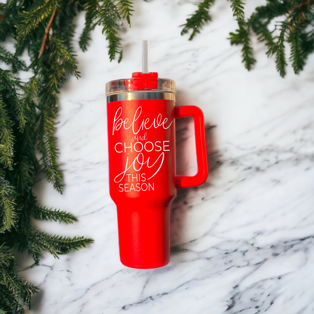 Believe + Joy 40oz insulated mug with a cheerful design and inspirational quote, featuring a lid, straw, and handle.