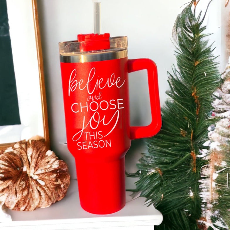 Believe + Joy 40oz insulated mug with a cheerful design and inspirational quote, featuring a lid, straw, and handle.