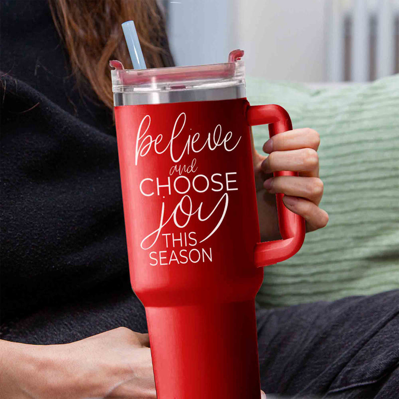 Believe + Joy 40oz insulated mug with a cheerful design and inspirational quote, featuring a lid, straw, and handle.