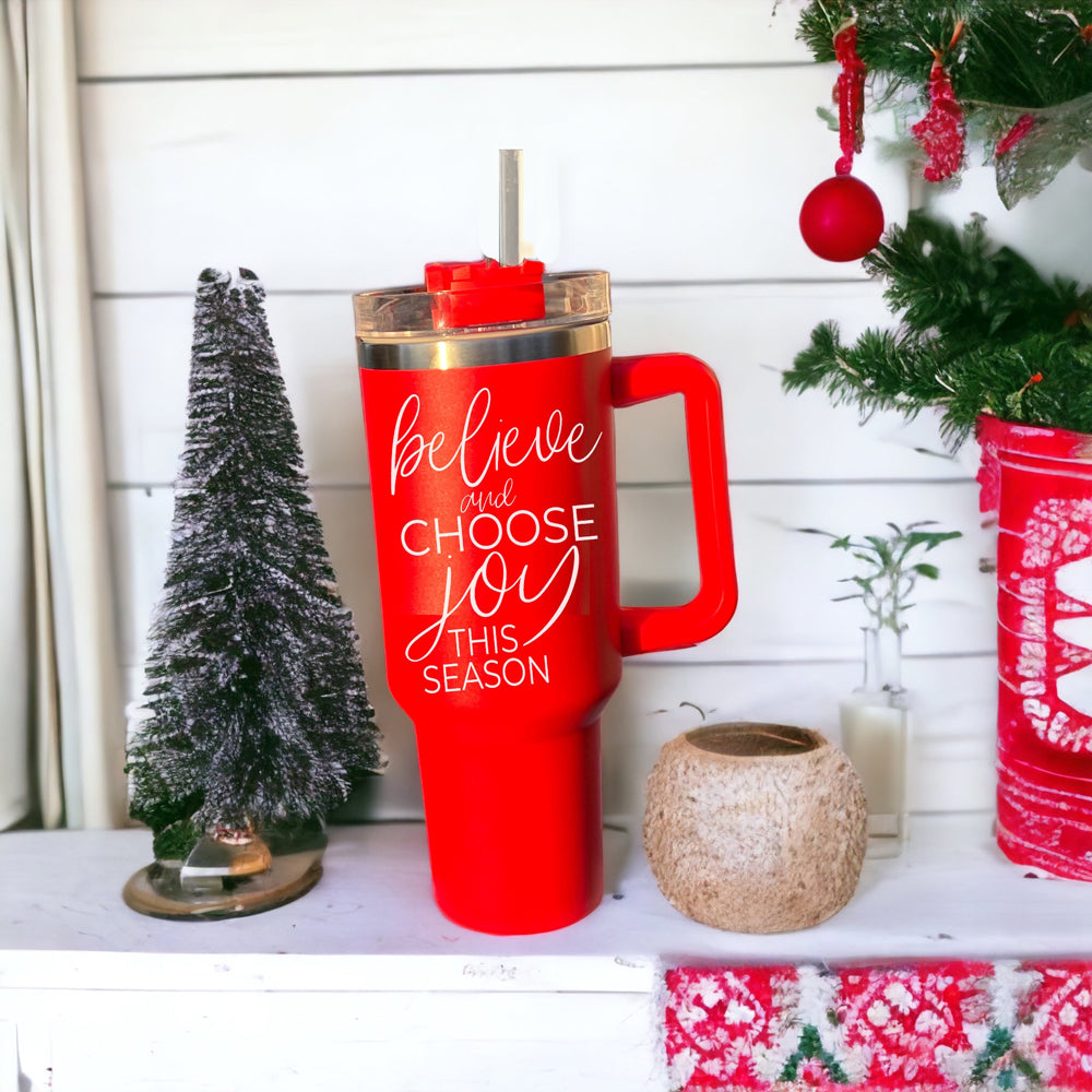 Believe + Joy 40oz insulated mug with a cheerful design and inspirational quote, featuring a lid, straw, and handle.