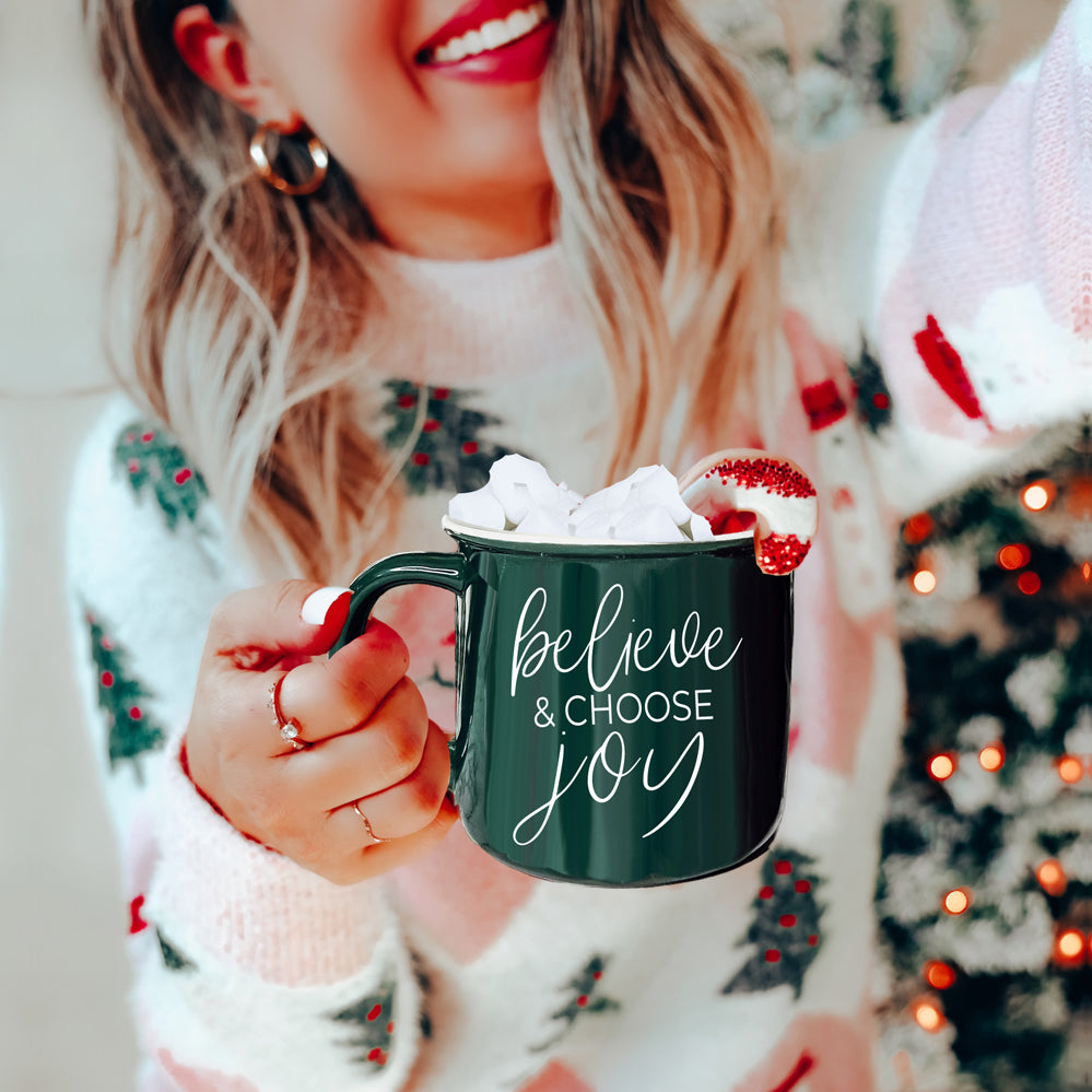 A ceramic Believe & Joy Mug in red with white lettering, featuring a positive message on both sides, perfect for holiday gifting.