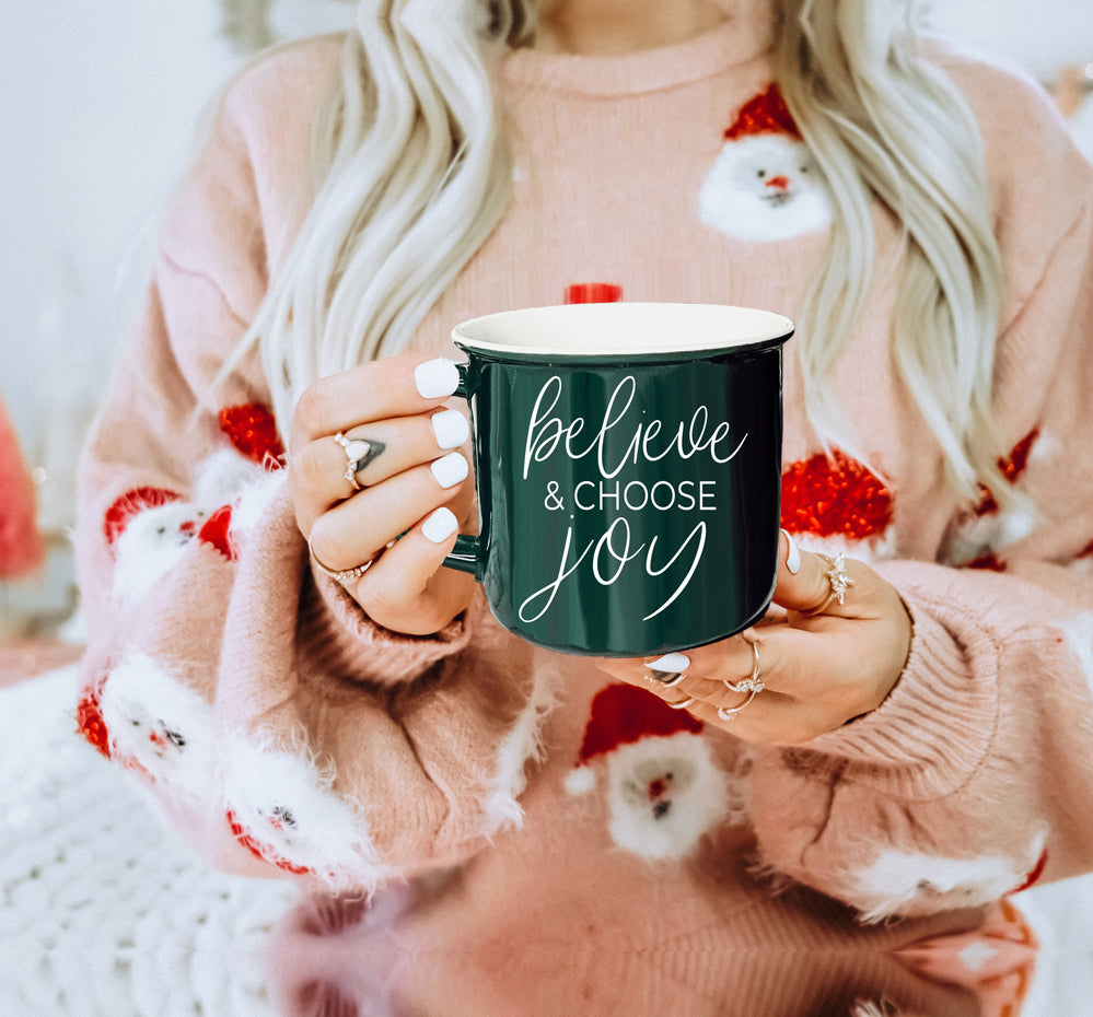 A ceramic Believe & Joy Mug in red with white lettering, featuring a positive message on both sides, perfect for holiday gifting.