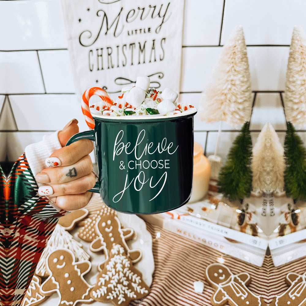 A ceramic Believe & Joy Mug in red with white lettering, featuring a positive message on both sides, perfect for holiday gifting.