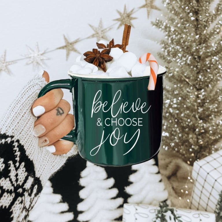 A ceramic Believe & Joy Mug in red with white lettering, featuring a positive message on both sides, perfect for holiday gifting.