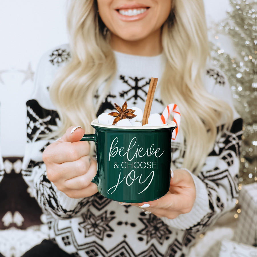 A ceramic Believe & Joy Mug in red with white lettering, featuring a positive message on both sides, perfect for holiday gifting.