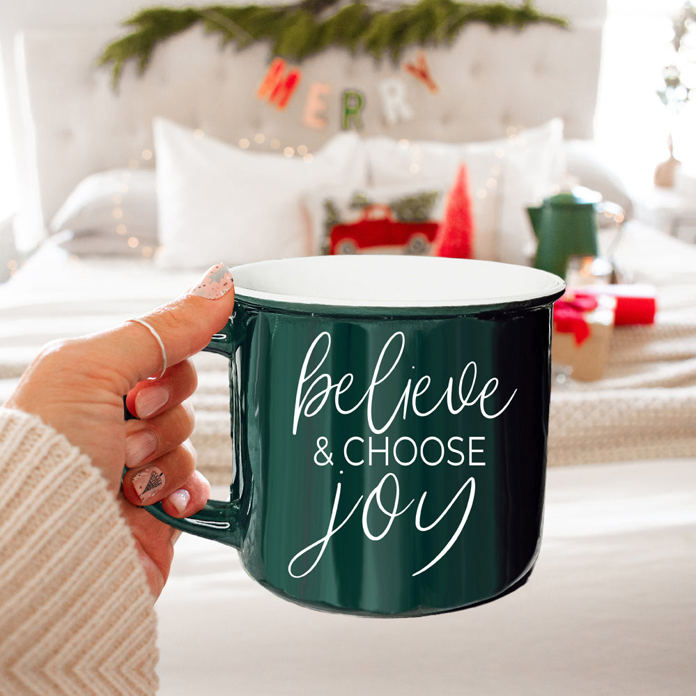 A ceramic Believe & Joy Mug in red with white lettering, featuring a positive message on both sides, perfect for holiday gifting.