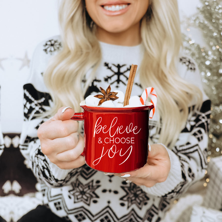 A ceramic Believe & Joy Mug in red with white lettering, featuring a positive message on both sides, perfect for holiday gifting.