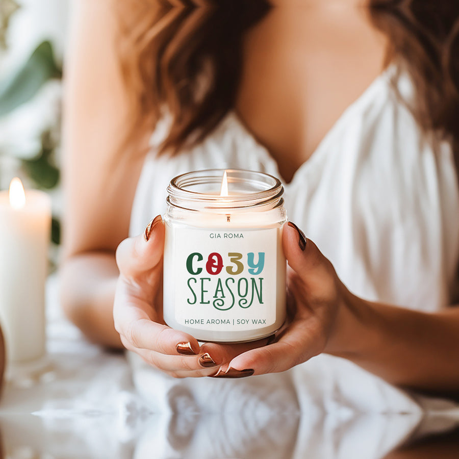 A beautifully crafted 9oz Cozy Season Candle with a warm glow, featuring a blend of winter scents like citrus, cloves, and pine cones.