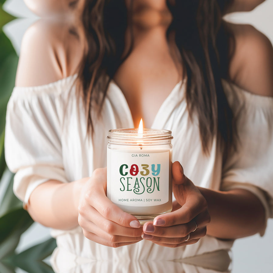 A beautifully crafted 9oz Cozy Season Candle with a warm glow, featuring a blend of winter scents like citrus, cloves, and pine cones.