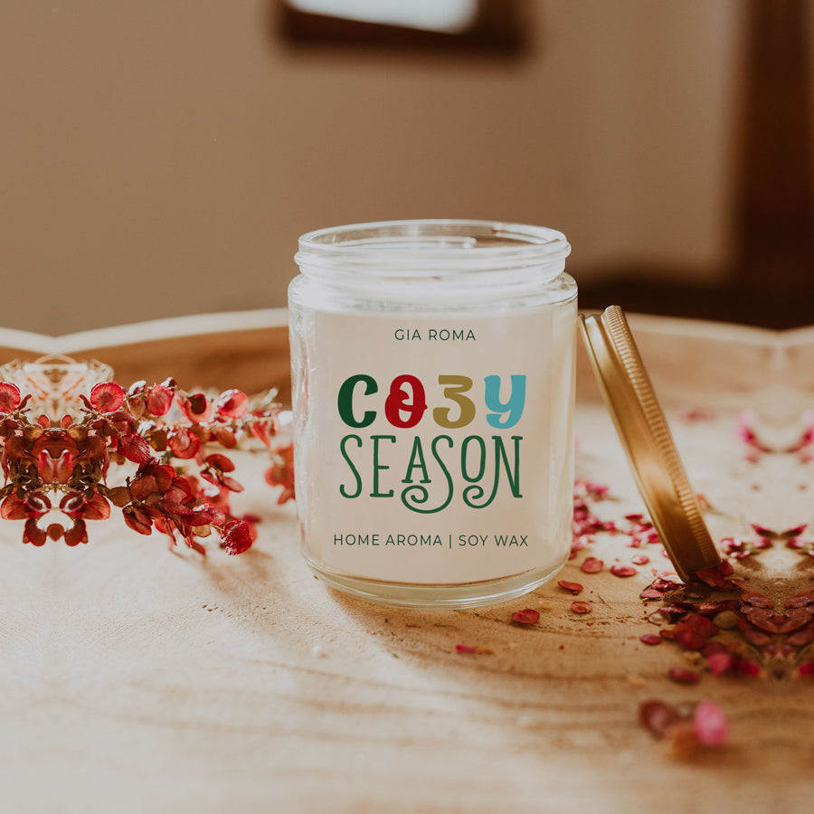 A beautifully crafted 9oz Cozy Season Candle with a warm glow, featuring a blend of winter scents like citrus, cloves, and pine cones.