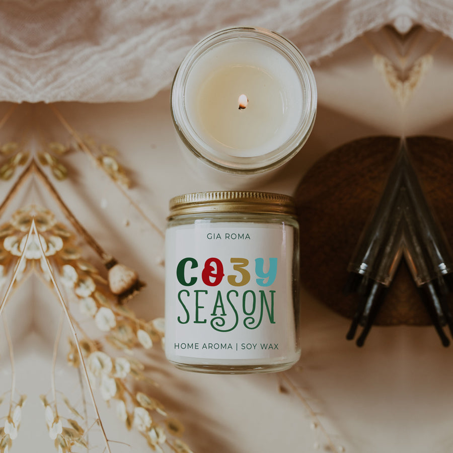 A beautifully crafted 9oz Cozy Season Candle with a warm glow, featuring a blend of winter scents like citrus, cloves, and pine cones.