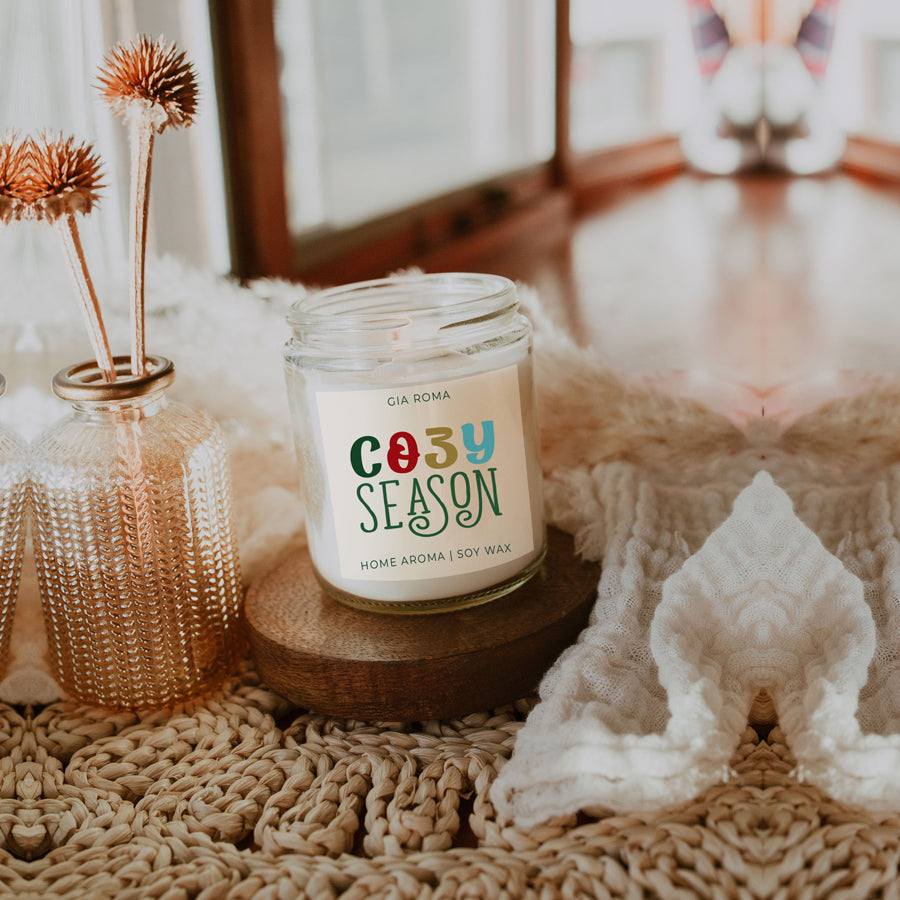 A beautifully crafted 9oz Cozy Season Candle with a warm glow, featuring a blend of winter scents like citrus, cloves, and pine cones.