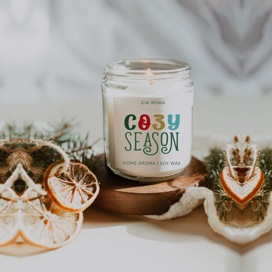 A beautifully crafted 9oz Cozy Season Candle with a warm glow, featuring a blend of winter scents like citrus, cloves, and pine cones.