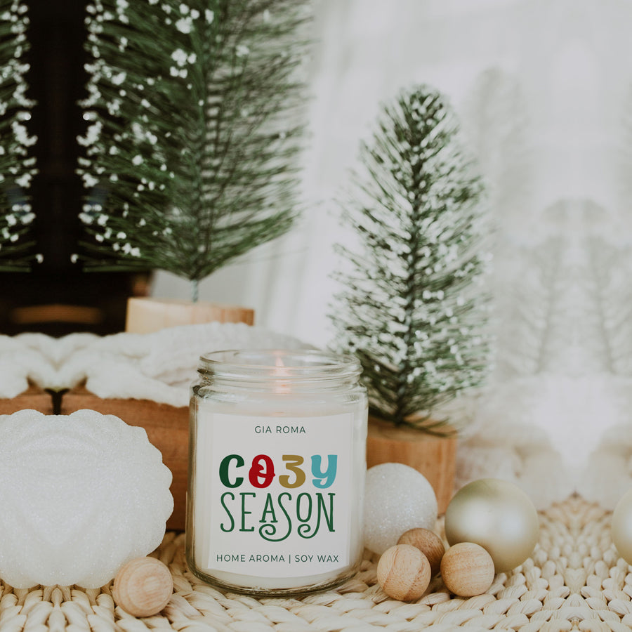 A beautifully crafted 9oz Cozy Season Candle with a warm glow, featuring a blend of winter scents like citrus, cloves, and pine cones.