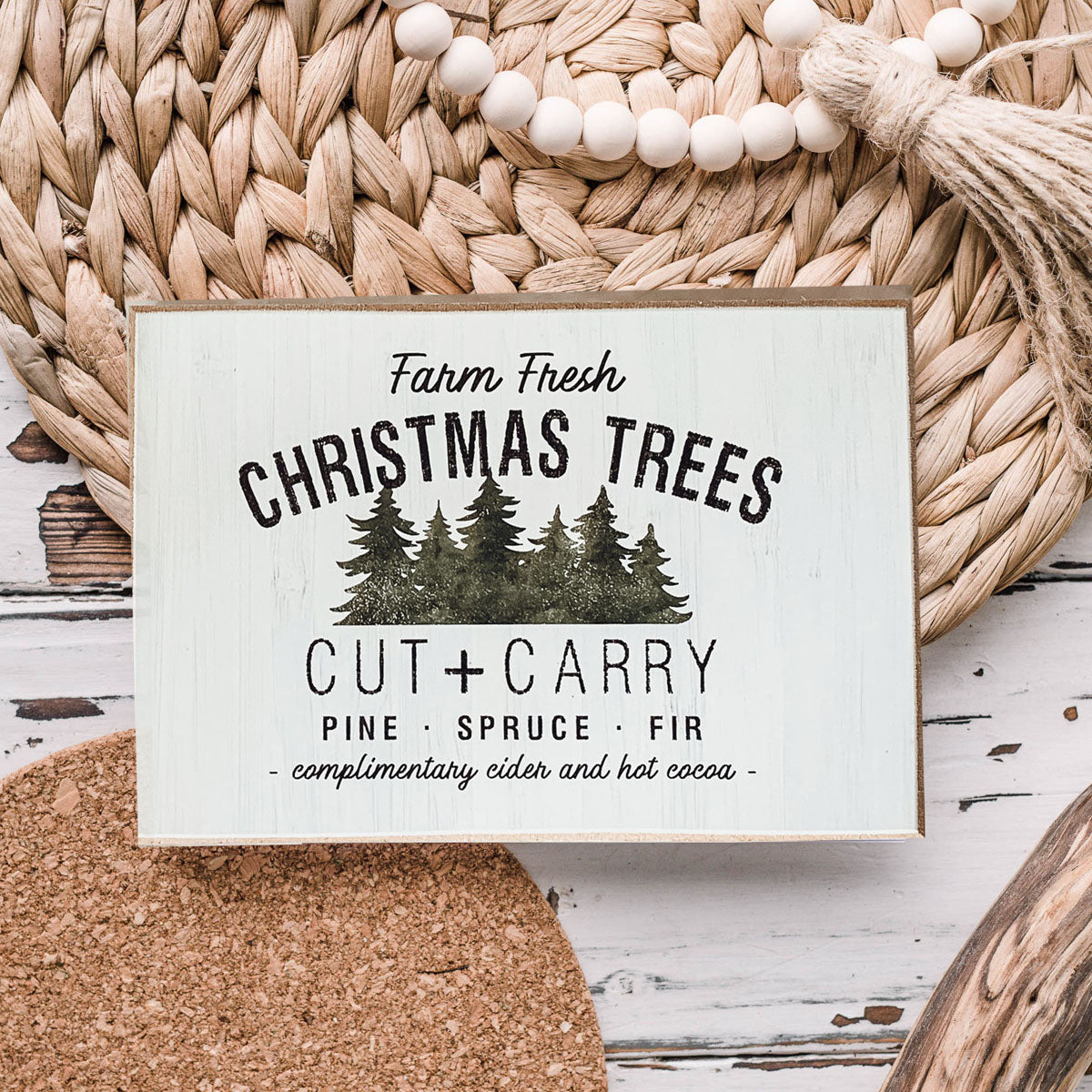 A decorative Cut + Carry Sign featuring a light gray textured background with the text about farm fresh Christmas trees and complimentary cider and hot cocoa.