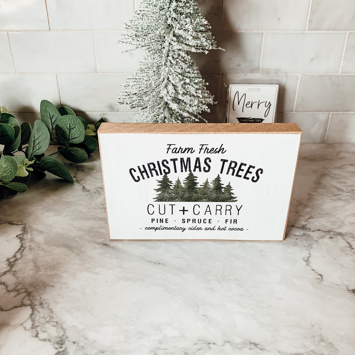 A decorative Cut + Carry Sign featuring a light gray textured background with the text about farm fresh Christmas trees and complimentary cider and hot cocoa.