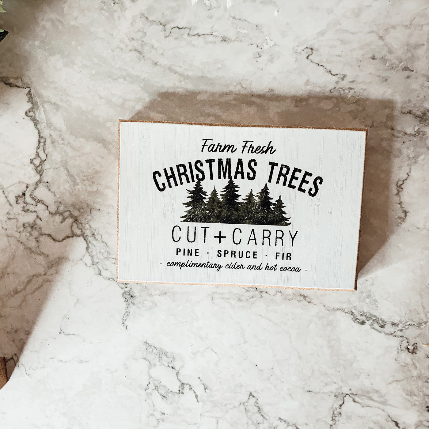 A decorative Cut + Carry Sign featuring a light gray textured background with the text about farm fresh Christmas trees and complimentary cider and hot cocoa.