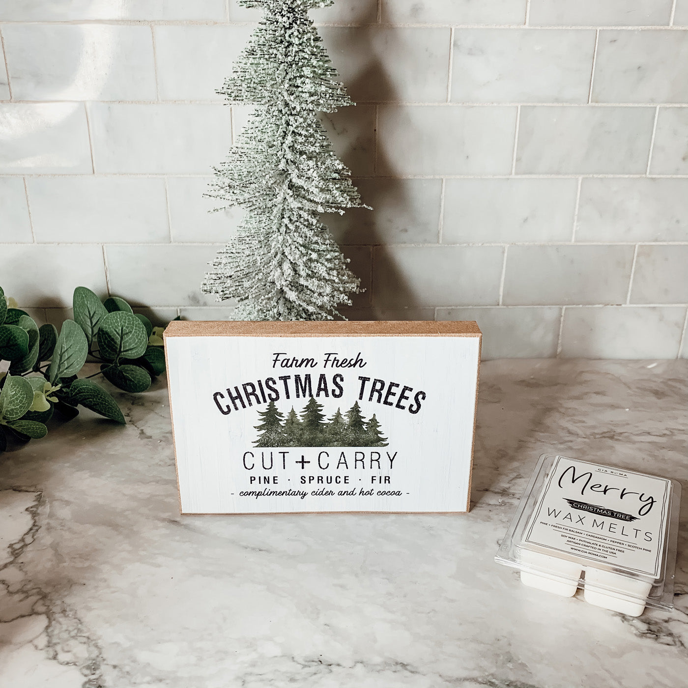 A decorative Cut + Carry Sign featuring a light gray textured background with the text about farm fresh Christmas trees and complimentary cider and hot cocoa.