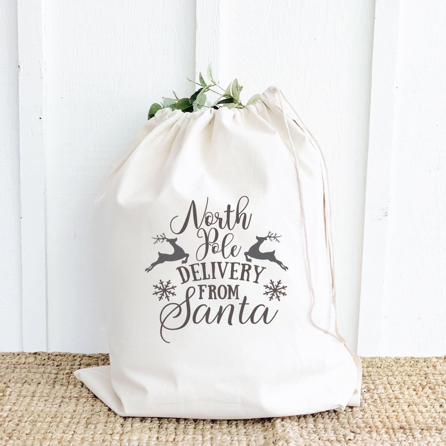 A festive Santa Sack made of heavy-duty canvas, featuring a drawstring closure and cotton webbing handle, perfect for carrying Christmas gifts.