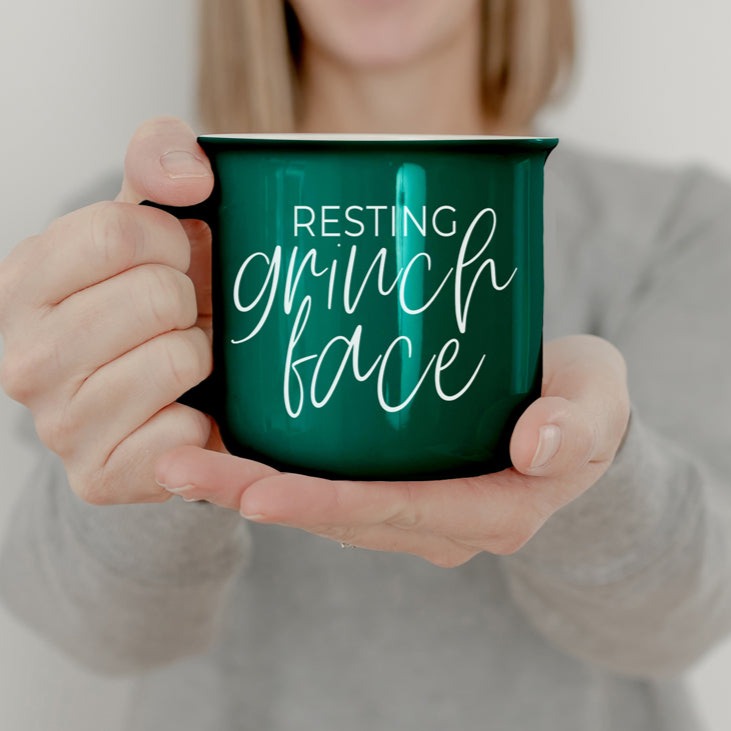 A whimsical Grinch Face Mug in red ceramic, featuring the Grinch's face and white lettering, perfect for holiday beverages.