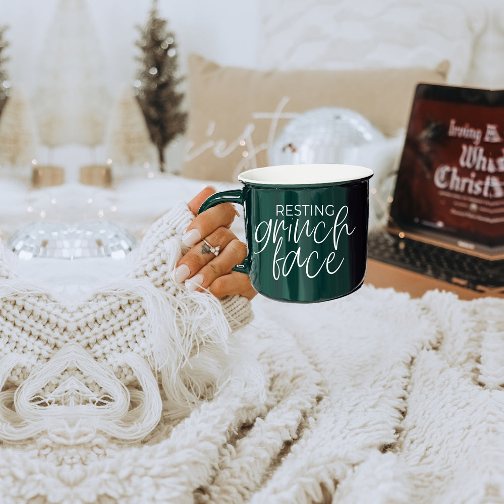 A whimsical Grinch Face Mug in red ceramic, featuring the Grinch's face and white lettering, perfect for holiday beverages.