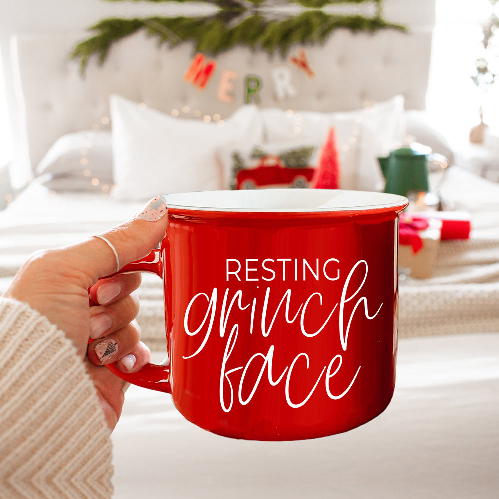 A whimsical Grinch Face Mug in red ceramic, featuring the Grinch's face and white lettering, perfect for holiday beverages.