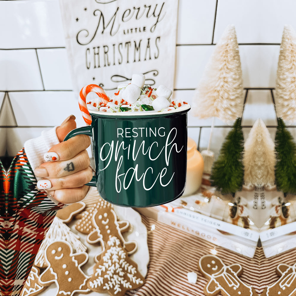 A whimsical Grinch Face Mug in red ceramic, featuring the Grinch's face and white lettering, perfect for holiday beverages.