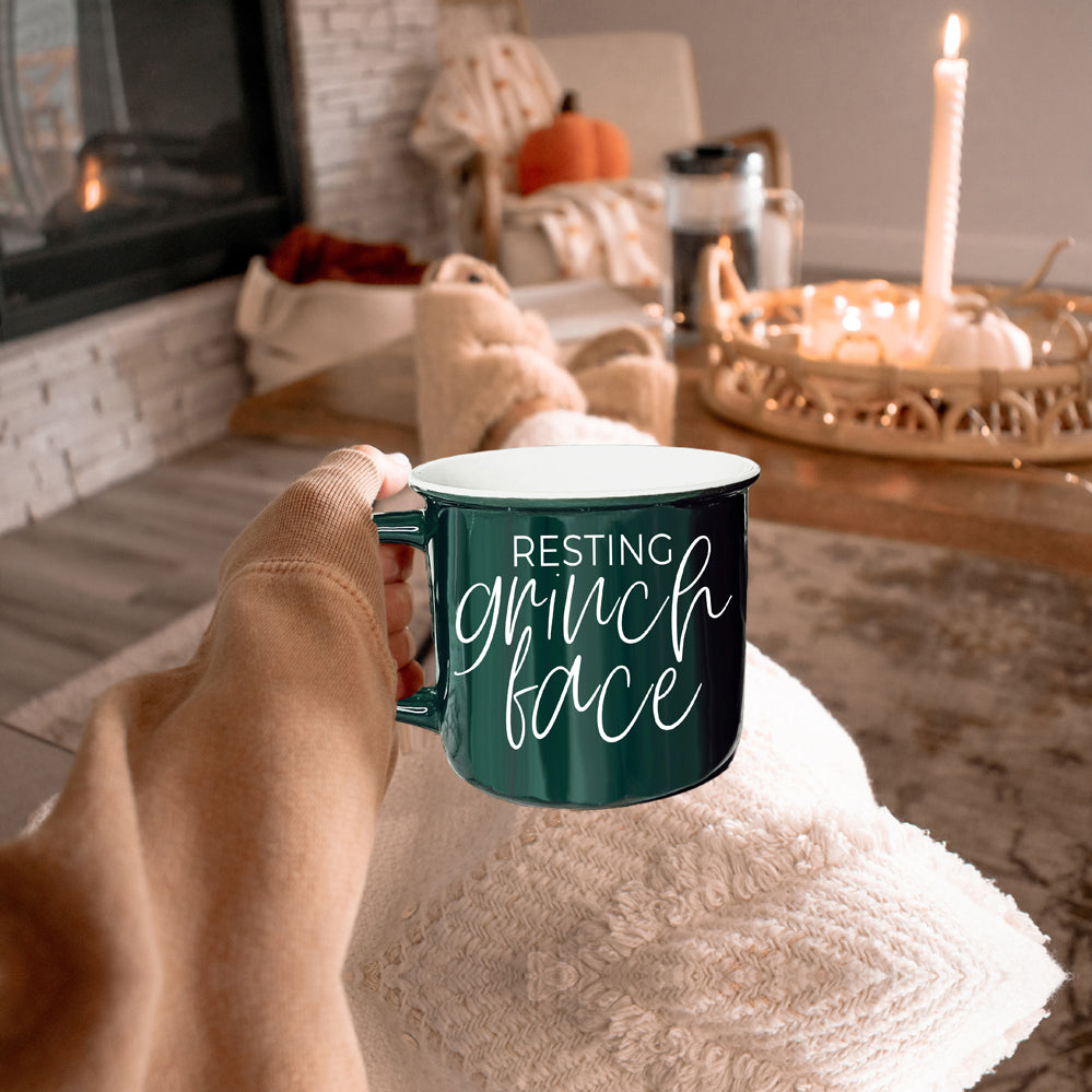 A whimsical Grinch Face Mug in red ceramic, featuring the Grinch's face and white lettering, perfect for holiday beverages.