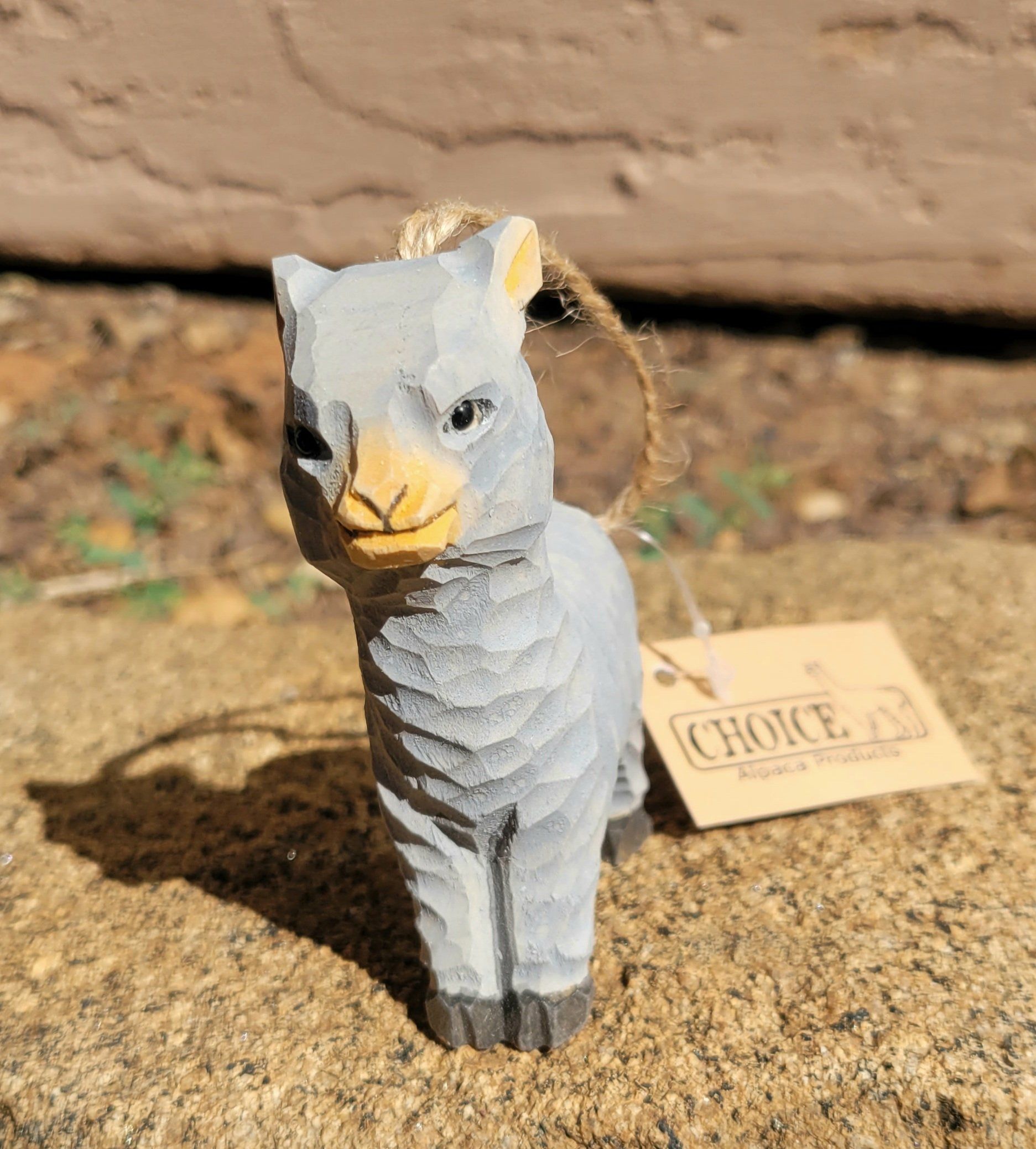 A set of hand-carved wooden alpaca ornaments made from basswood, featuring friendly smiling faces and textured fleecy coats, with jute hanging cords.