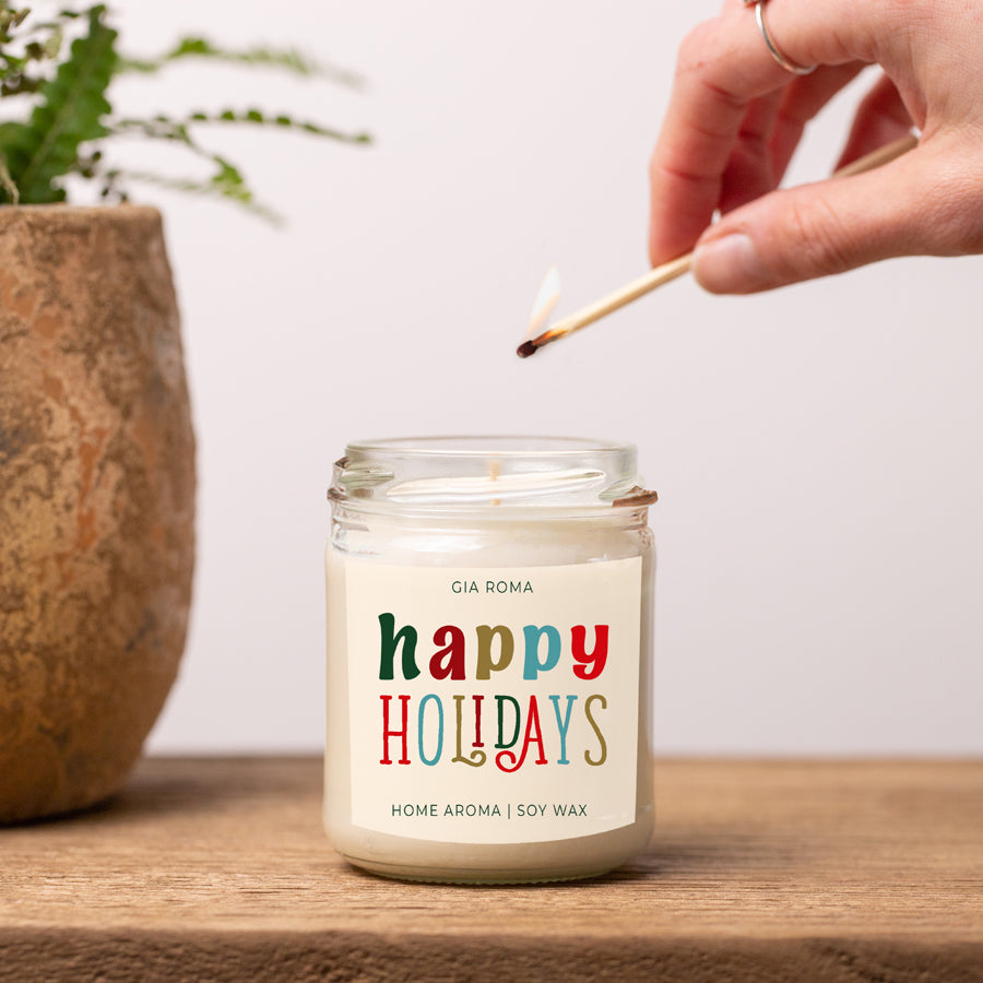 Happy Holiday Candle in a 9oz jar with festive scents of pine, orange, and woods, perfect for creating a cozy holiday atmosphere.