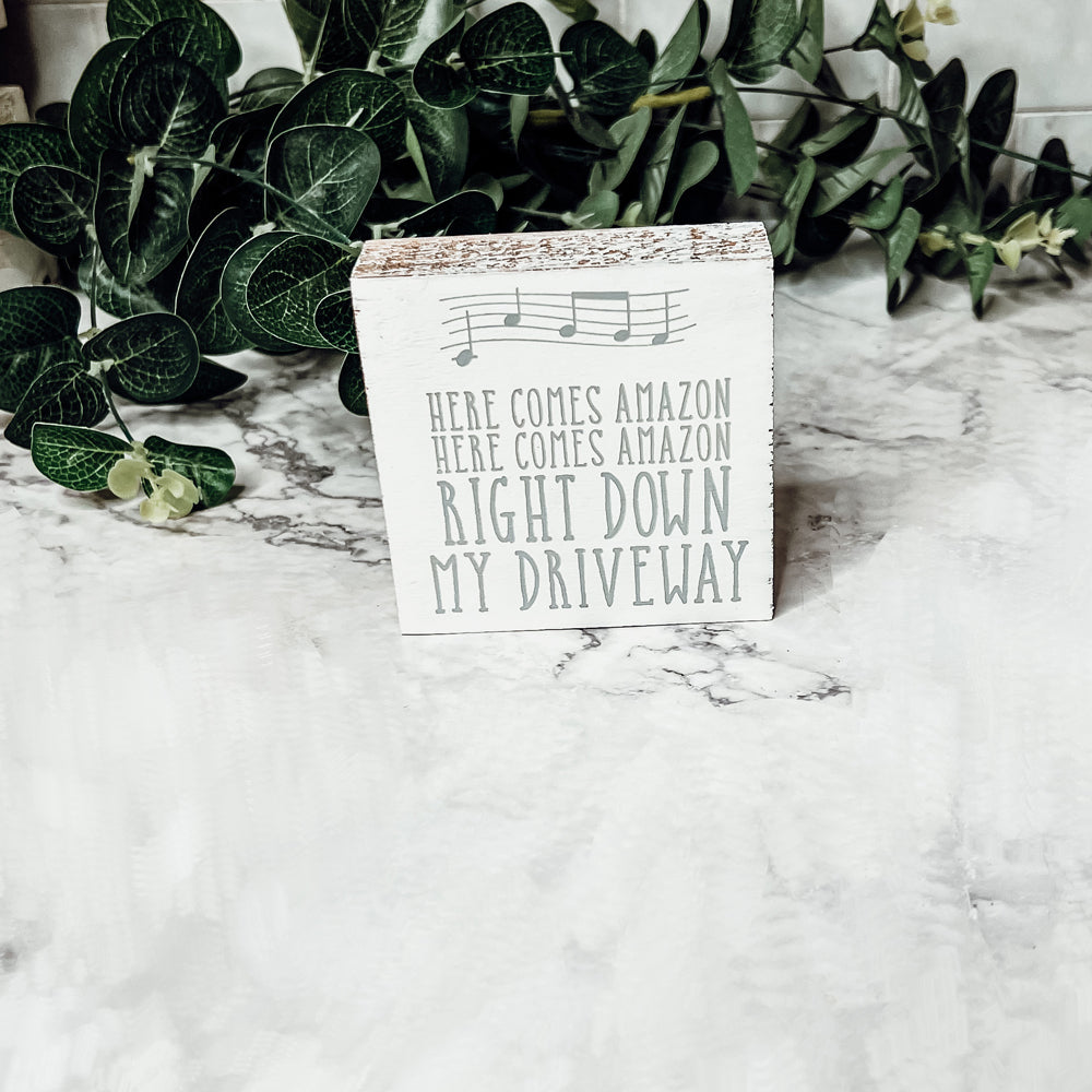 A charming wooden block sign that reads 'Here Comes Amazon' in neutral colors, perfect for home decor.