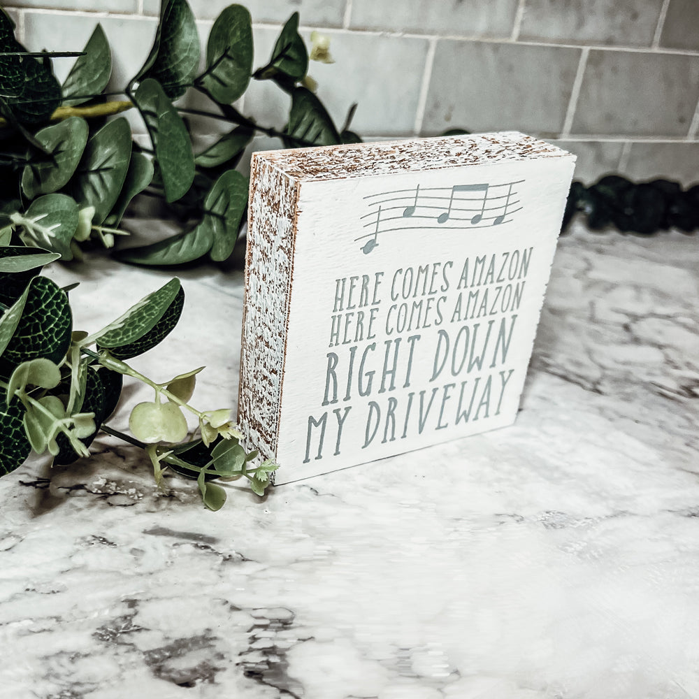 A charming wooden block sign that reads 'Here Comes Amazon' in neutral colors, perfect for home decor.