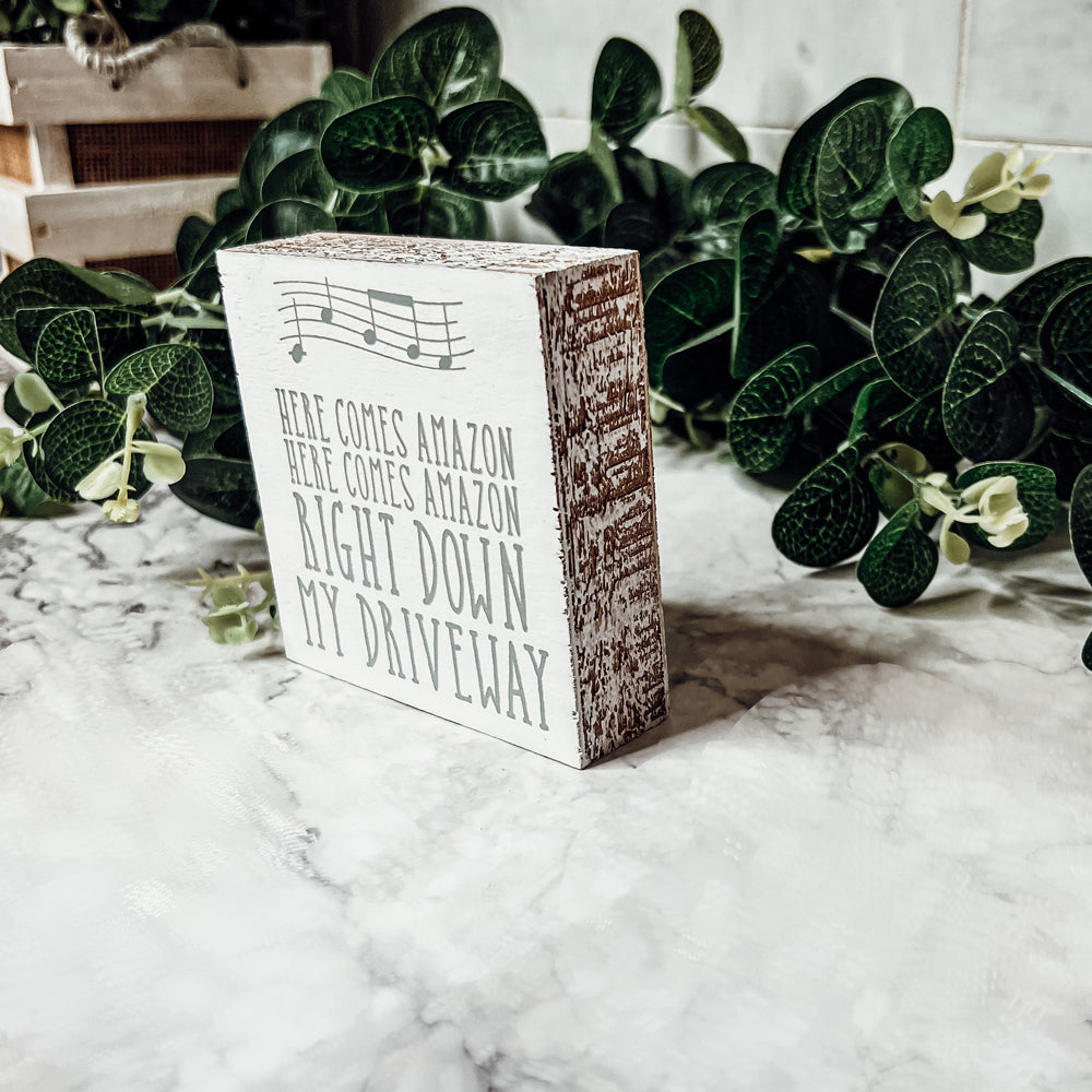 A charming wooden block sign that reads 'Here Comes Amazon' in neutral colors, perfect for home decor.