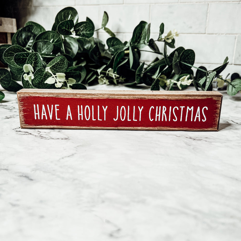 Holly Jolly Sitter Sign, a wooden block sign with festive lettering, perfect for holiday decor.