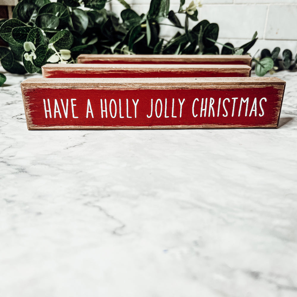 Holly Jolly Sitter Sign, a wooden block sign with festive lettering, perfect for holiday decor.