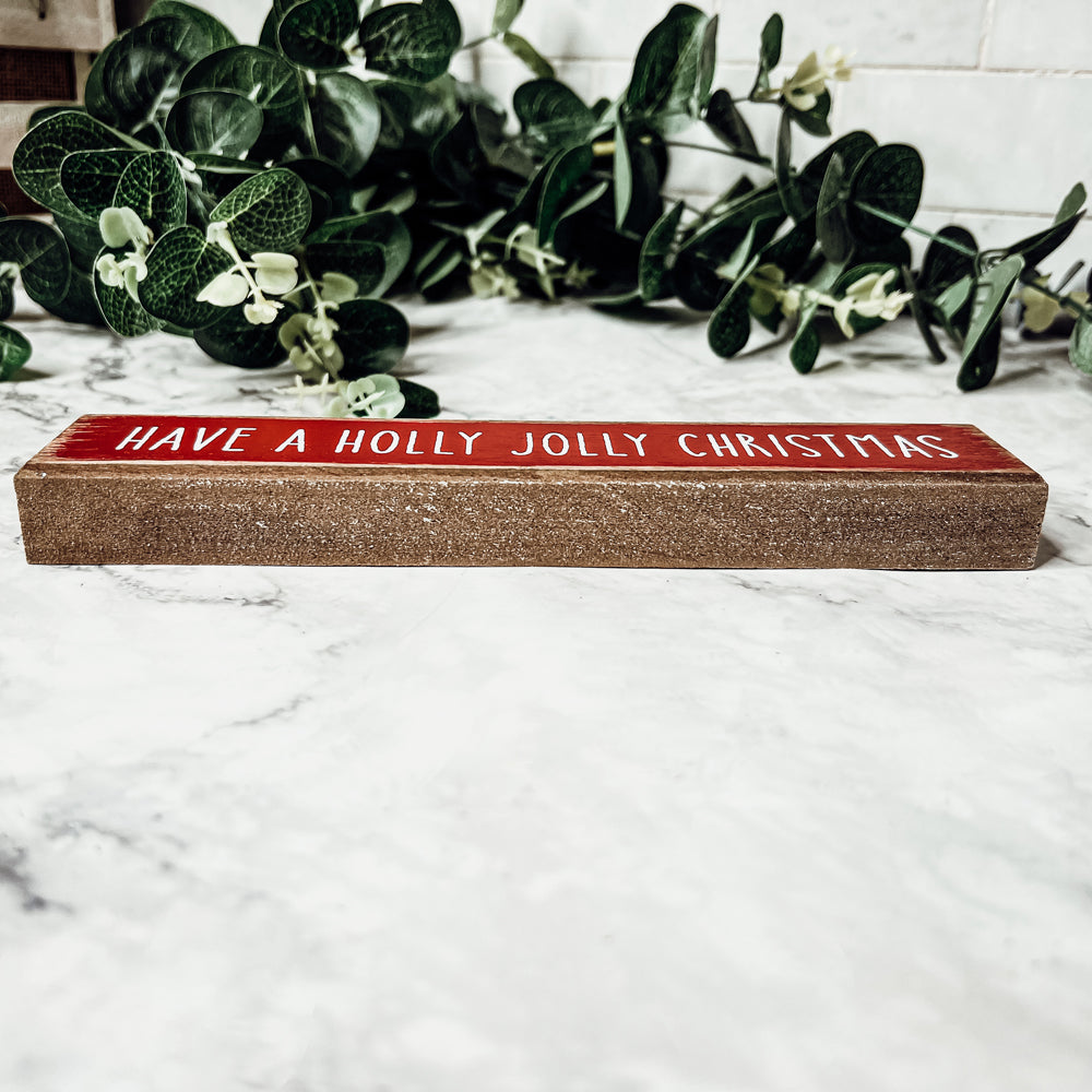 Holly Jolly Sitter Sign, a wooden block sign with festive lettering, perfect for holiday decor.